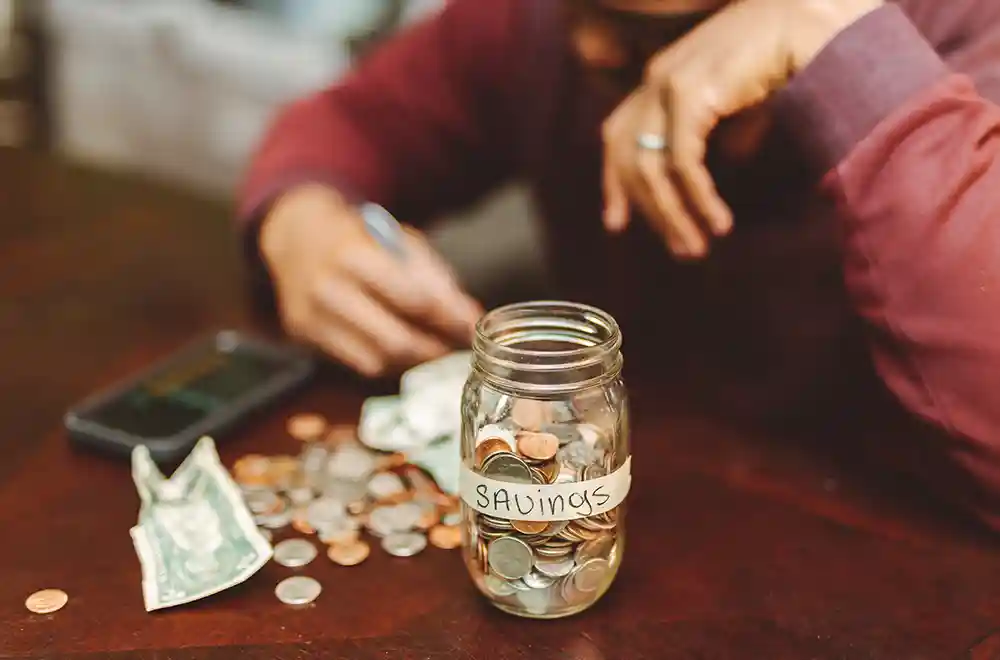 savings jar with person counting money on desk